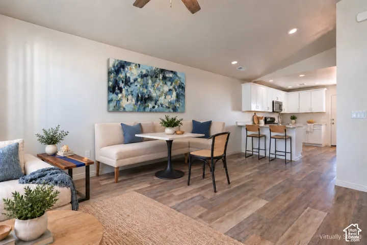 Open-concept interior featuring wood-finish flooring, vaulted ceilings with a recessed lighting package, and a kitchen equipped with white cabinetry and a built-in breakfast bar