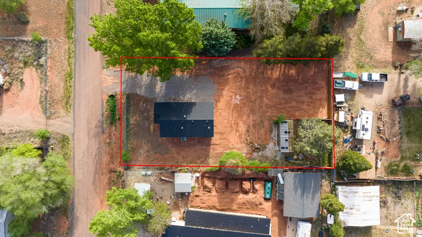 Aerial perspective of a property featuring a rectangular lot, mature trees, a gravel driveway, and an established building footprint