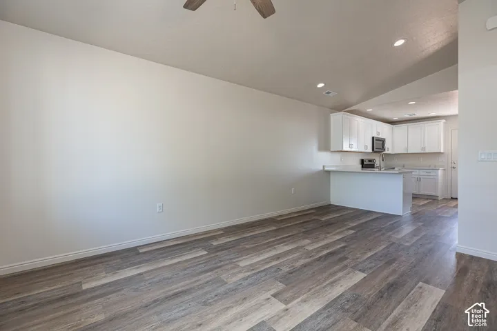 Open-concept interior featuring vaulted ceilings, wood-finish flooring, recessed lighting, and a kitchen equipped with white cabinetry and a breakfast bar