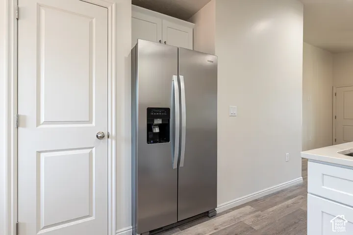 Stainless steel side-by-side refrigerator, white shaker-style cabinetry, wood-finish flooring, and crisp white panel doors