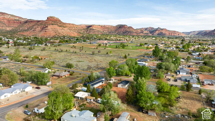 Aerial perspective featuring expansive desert terrain, mature native trees, and prominent red rock mountain formations