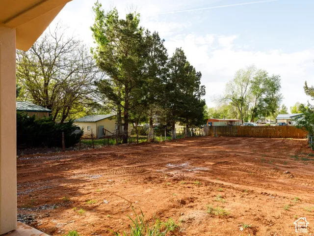 Covered back patio overlooking an expansive lot with mature trees, perimeter fencing, and a detached greenhouse structure