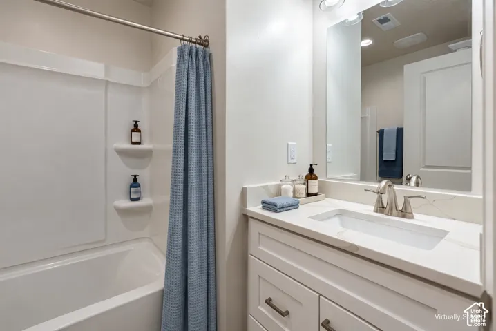Bathroom featuring a white vanity cabinet with a stone-composite countertop, an integrated rectangular sink, a brushed-nickel faucet, and a wall-to-wall mirror with a tub-shower combination