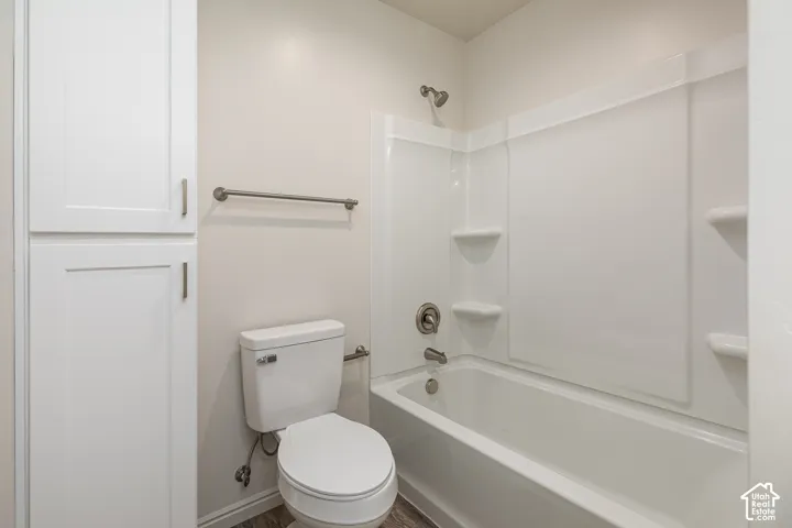 Bathroom featuring a shower and tub combination with integrated shelving, white cabinetry, a neutral toilet, and metal hardware finishes