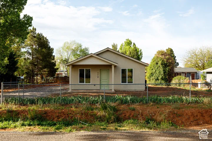 Fully fenced yard -Single-story residence featuring light-toned stucco siding, a covered front entryway, double-pane windows, and chain-link perimeter fencing