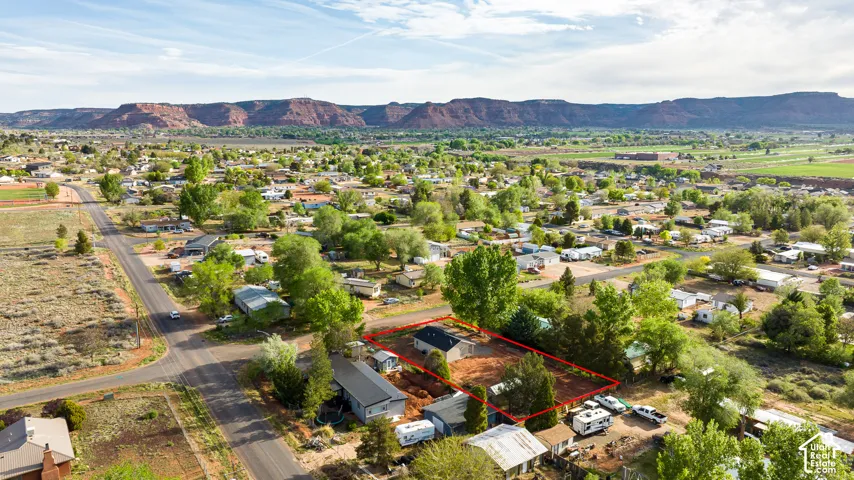Aerial perspective of a residential lot featuring red earth terrain, mature shade trees, and a mountain backdrop