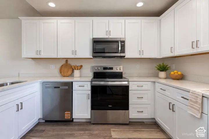 Kitchen featuring white shaker-style cabinetry, quartz countertops, stainless steel appliances, and wood-finish flooring