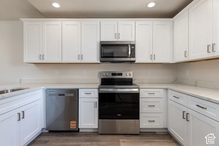 Kitchen featuring white shaker-style cabinetry, light-toned stone-finish countertops, stainless steel appliances, and wood-finish flooring