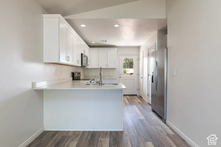 Kitchen featuring white shaker-style cabinetry, a peninsula with stone-finish countertops, stainless steel appliances, and wood-finish flooring