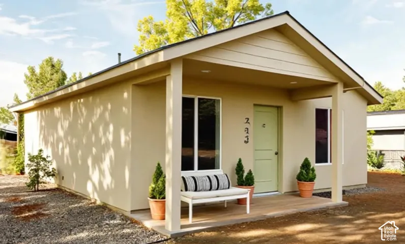 Exterior featuring a covered front porch with wood-finish decking, smooth stucco siding, a gable roofline, and dual-pane windows