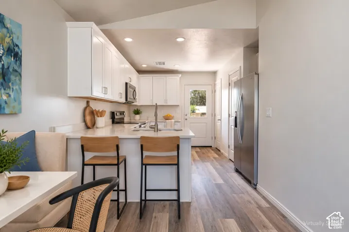 Kitchen featuring white cabinetry, solid surface countertops, recessed lighting, wood-finish flooring, and stainless steel refrigerator