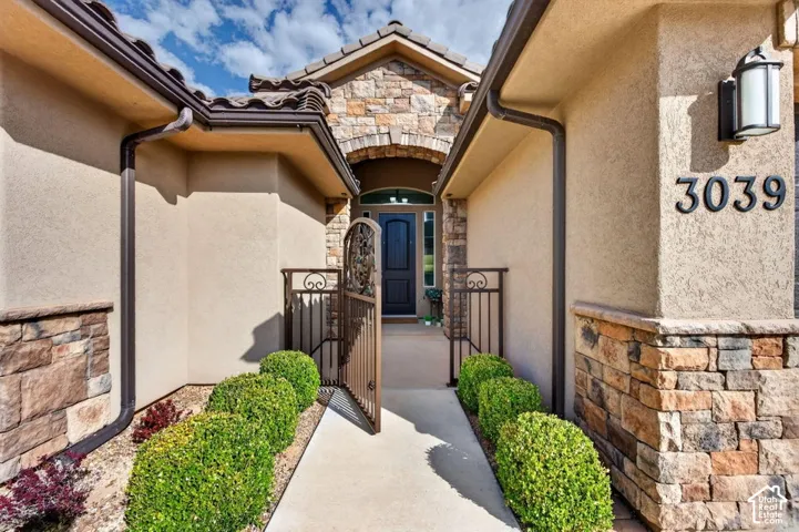 Stucco exterior with stone veneer accents, decorative metal courtyard gate, tiled roof, and wall-mounted exterior lighting