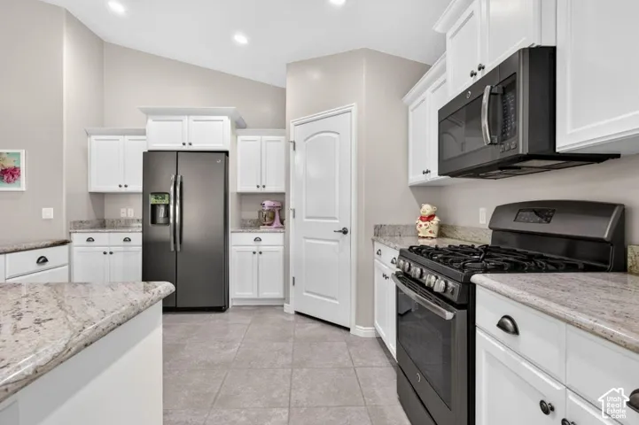 Kitchen featuring white cabinetry, stone countertops, dark-finish appliances, tile flooring, and vaulted ceilings