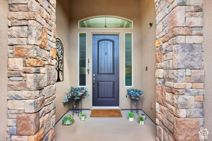 Covered entry featuring natural stone columns, a paneled solid wood door, sidelights, and an arched transom window