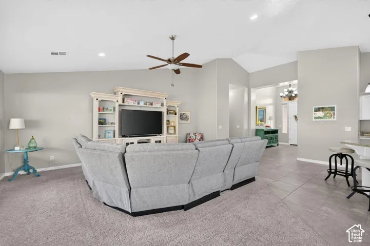 Vaulted ceiling featuring a central lighted ceiling fan, custom built-in entertainment center with open shelving, and neutral tone tile flooring