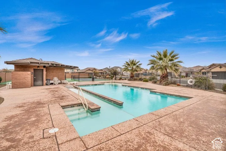 In-ground swimming pool featuring a built-in spa, concrete patio, palm trees, and an enclosed hardscape area