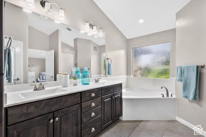 Dual-sink vanity with dark wood-finish cabinetry, solid-surface countertop, full-width wall mirror, and built-in soaking tub with a metal deck-mounted faucet