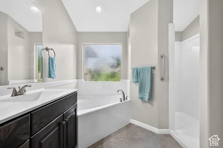 Dark-toned vanity with a white countertop and integrated sink, soaking tub with a privacy-glass window, and walk-in shower with tile flooring