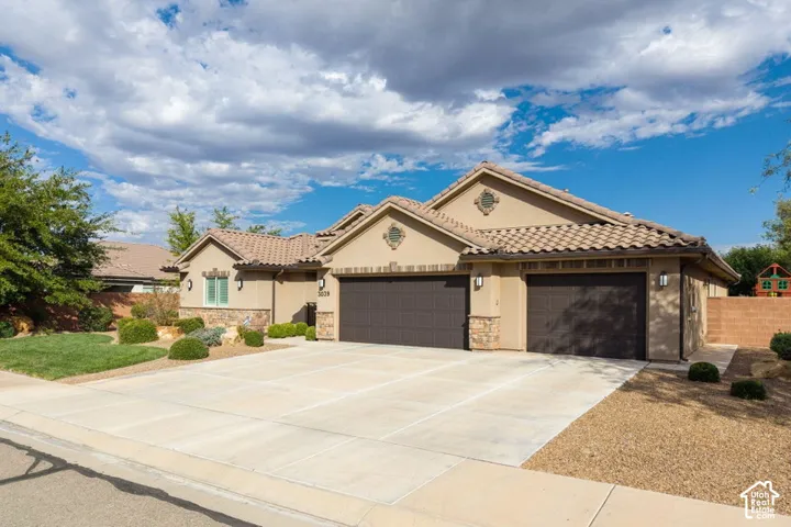 Stucco exterior with stone veneer accents, multi-gabled tile roof, and a three-car garage featuring segmented roll-up doors