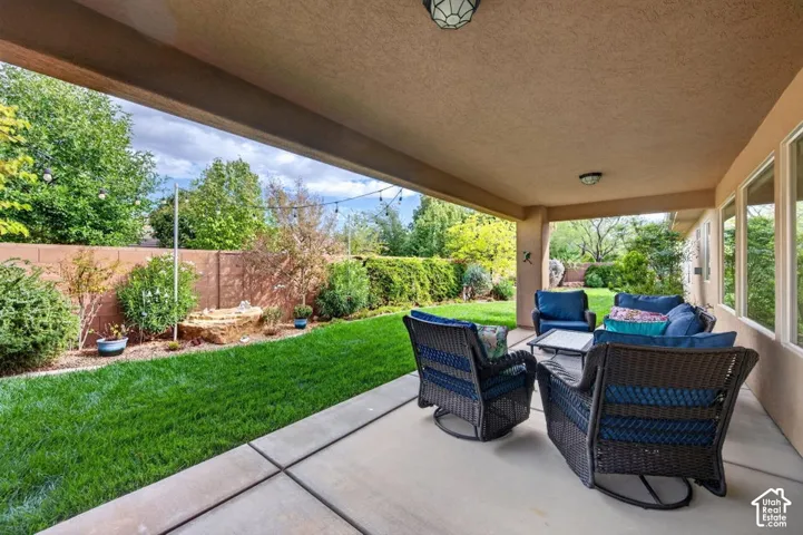 Covered concrete patio with overhead lighting, expansive manicured lawn, masonry privacy wall, and mature landscaping
