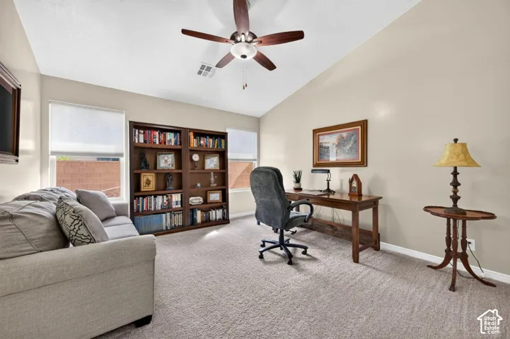 Vaulted ceilings, built-in wooden shelving, neutral carpeting, and a ceiling fan with integrated lighting