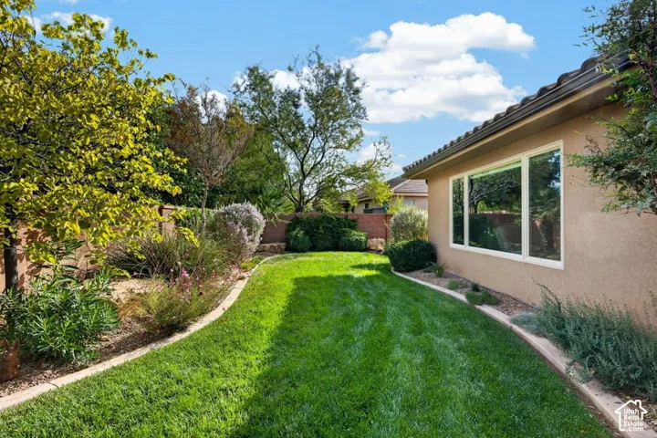 Backyard featuring a manicured lawn, established landscaping, stone-edged garden beds, and a masonry perimeter wall