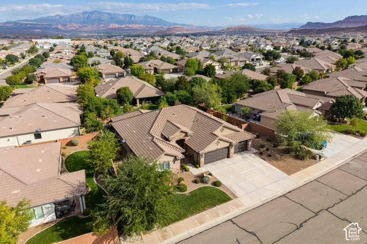 Aerial perspective of a single-story residence featuring a concrete tile roof, multi-car garage, manicured turf landscaping, and mountainous surroundings