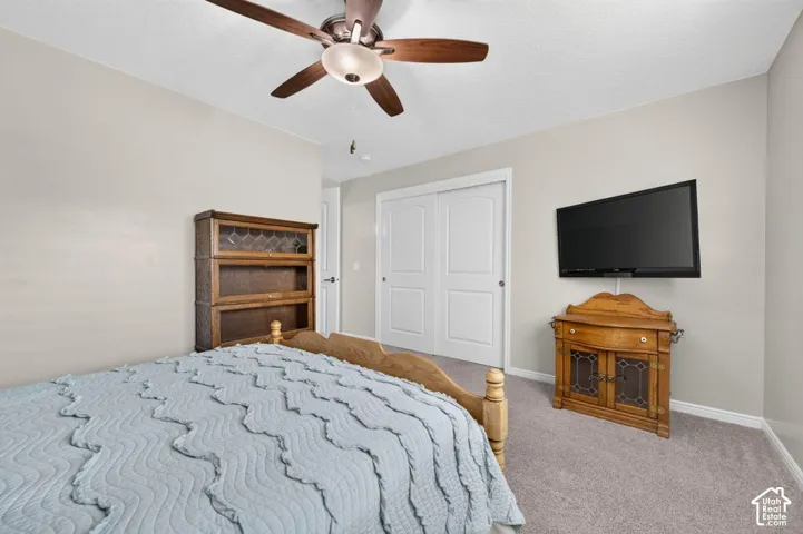 Bedroom featuring neutral wall paint, carpeted flooring, a ceiling fan with integrated lighting, and a double-door closet