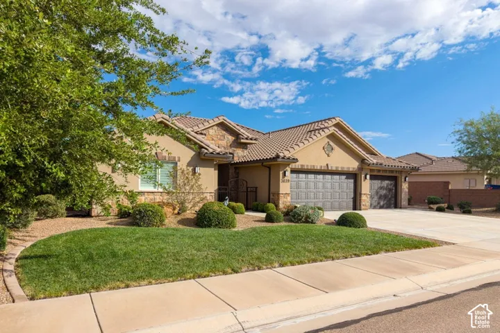 Stucco and stone exterior featuring a multi-gable roofline, attached three-car garage, and landscaped front lawn