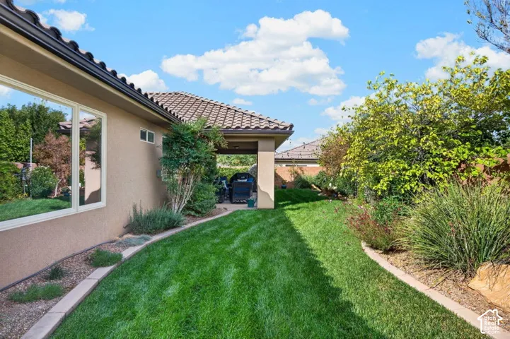 Stucco exterior featuring a covered patio, tile roof, manicured lawn, and stone-edged landscaping beds