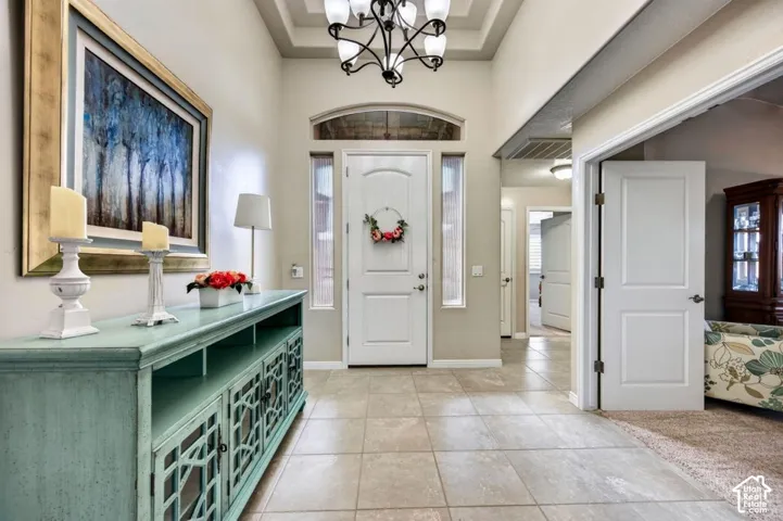 Entryway featuring a coffered ceiling, tile flooring, an arched glass-paneled front door with side windows, and a multi-light chandelier