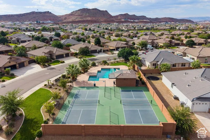 Aerial perspective featuring twin tennis courts, a structured swimming pool, a covered pavilion, and surrounding mountain scenery