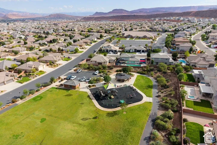 Community park featuring a paved walking path, open grass lawn, shaded pavilion, and integrated playground equipment