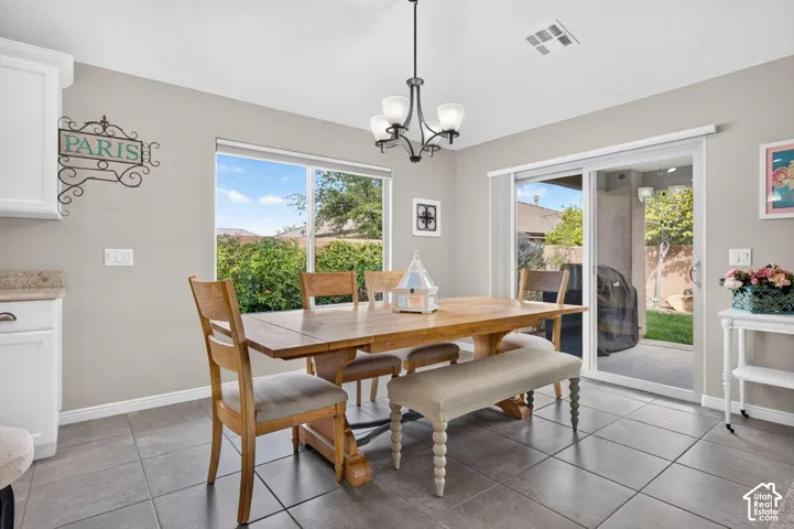 Dining area featuring large-format tile flooring, white cabinetry, a multi-light chandelier, a picture window, and a sliding glass door