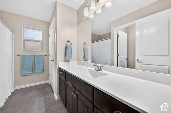 Dark-finish cabinetry, solid-surface countertop with integrated basin, polished chrome hardware, large-format tile flooring, and oversized wall-mounted mirror