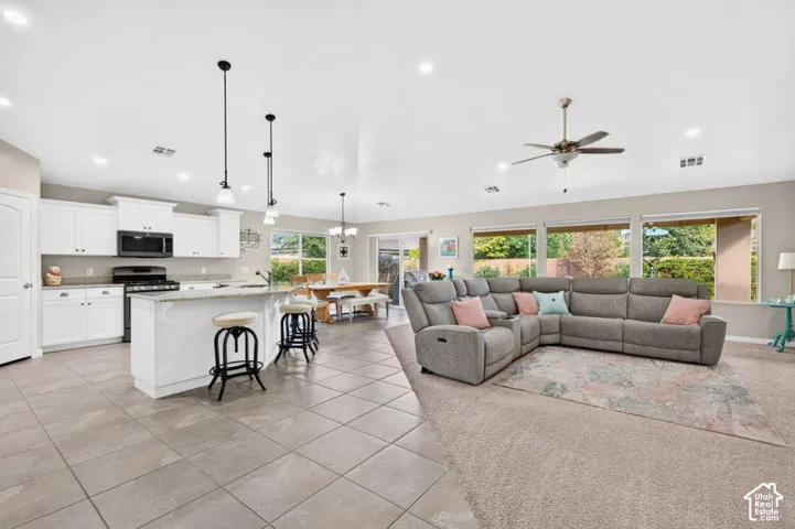 Open-concept floor plan featuring tile flooring, white shaker-style cabinetry, stone countertops, pendant lighting, and a ceiling fan
