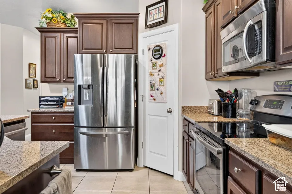 Kitchen featuring dark-toned cabinetry, stone-finish countertops, stainless steel appliances, and tiled flooring