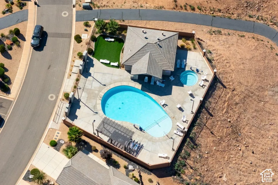 Aerial view featuring an expansive concrete patio, a custom-shaped swimming pool, an integrated spa, a pergola, and a synthetic turf lawn