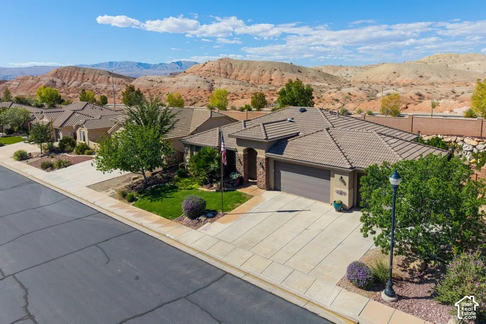 Single-story residence featuring a tile roof, multi-car garage, concrete driveway, and xeriscaped front landscape set against a mountain backdrop