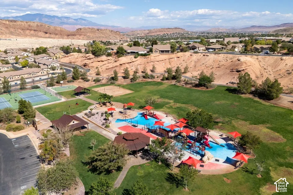 Community recreational area featuring a splash pad with shade structures, tennis courts, sand volleyball court, and covered pavilion set against a mountain backdrop