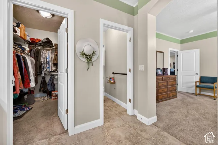 Interior hallway featuring ceramic tile flooring, arched wall detailing, neutral wall paint with decorative crown molding, and two-panel interior doors