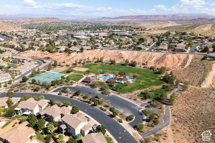 Aerial perspective of a community featuring a swimming pool, tennis courts, expansive green space, paved parking area, and multi-use paved pathways