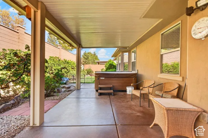 Covered concrete patio featuring a permanent spa, earth-tone stucco exterior, metal support columns, and perimeter masonry wall