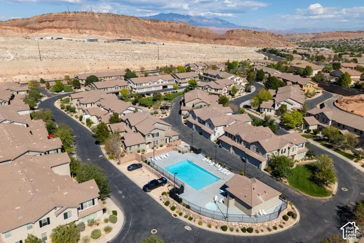 Aerial view of the community featuring an outdoor swimming pool, paved streets, landscaped grounds, and a mountain backdrop
