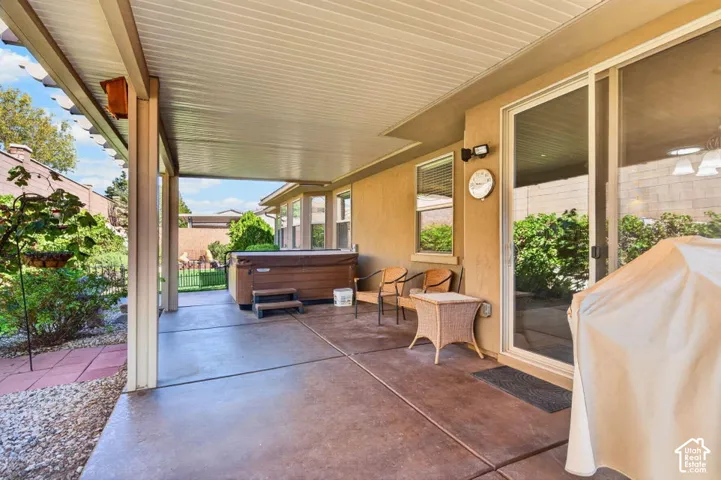 Covered concrete patio featuring an integrated hot tub, sliding glass door access, and professional hardscaping