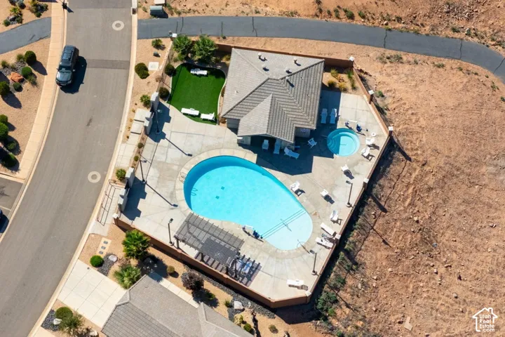 Aerial view featuring an expansive concrete patio, a custom-shaped swimming pool, an integrated spa, a pergola, and a synthetic turf lawn