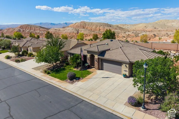 Single-story residence featuring a tile roof, multi-car garage, concrete driveway, and xeriscaped front landscape set against a mountain backdrop