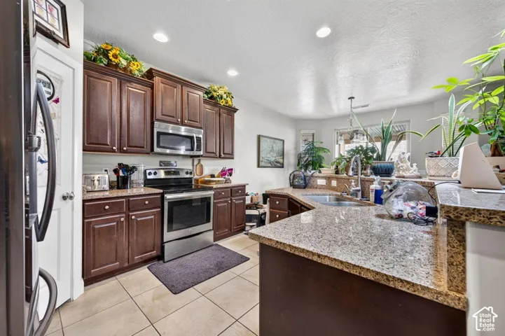 Kitchen featuring dark wood cabinetry, speckled stone countertops, stainless steel appliances, ceramic tile flooring, and recessed lighting