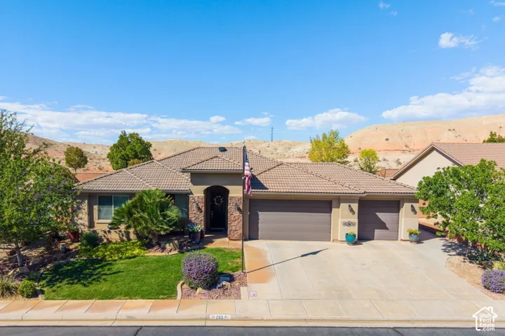 Single-story residence featuring a tile roof, stone masonry accents, a three-car garage, and landscaped front yard