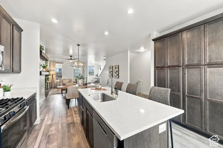 Kitchen featuring an expansive island with a stainless steel sink, wood-finish flooring, recessed lighting, and ample cabinetry